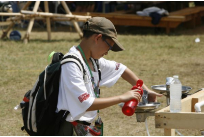 Scout in white t-shirt refills red reusable water bottle at a water fountain.