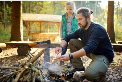 a father starting a campfire with his daughter.