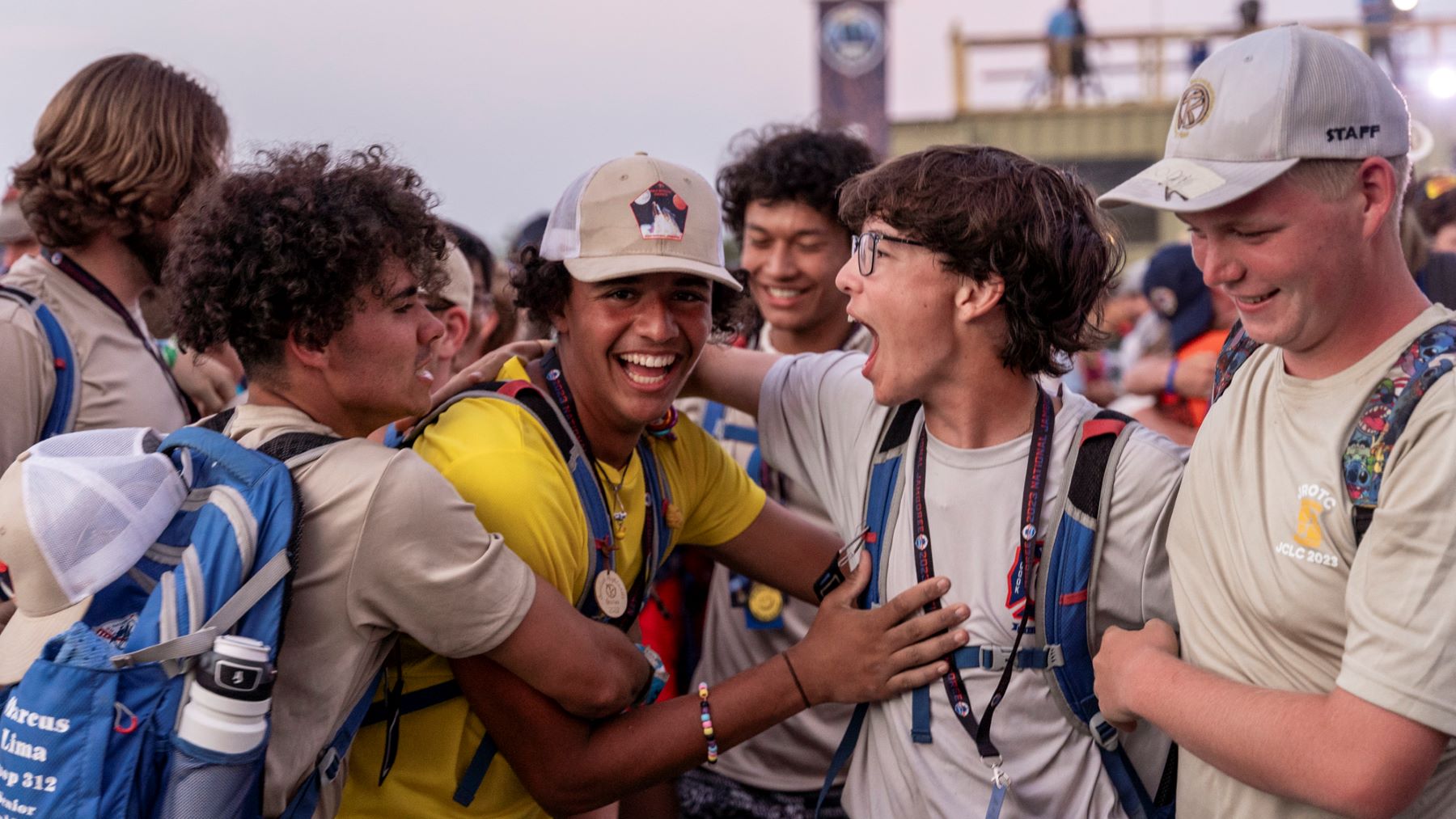 Group of Scouts smiling and laughing together at the National Jamboree, wearing backpacks and caps as they celebrate outdoors.