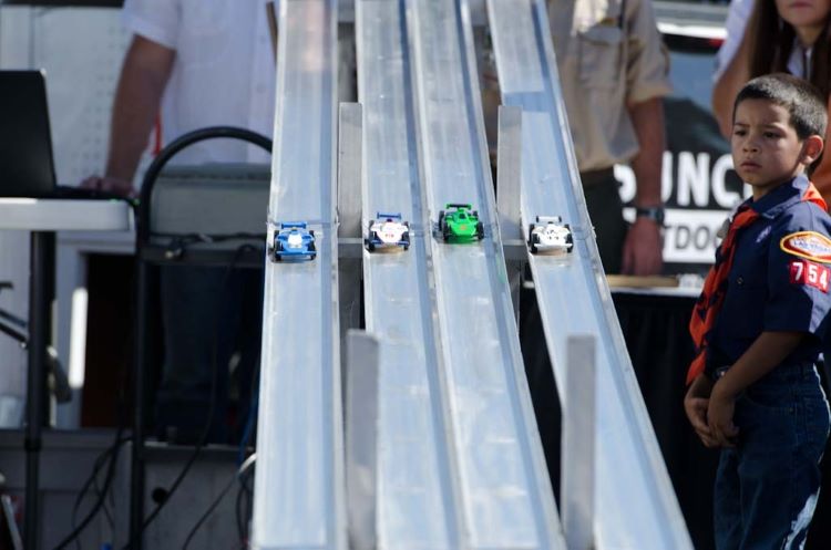 Pinewood Derby Cub Scout watches on as his Pinewood Derby car races on a metal track at a Pinewood Derby race.