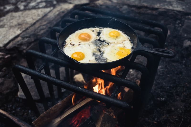 Eggs frying in a cast iron skillet over a campfire.