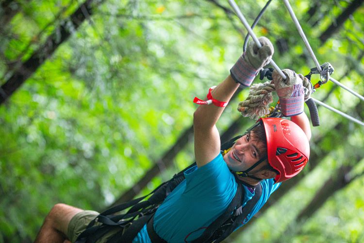 Scouts Zip-Lines Summit Scout wearing a blue shirt and red helmet zip-lines in West Virginia