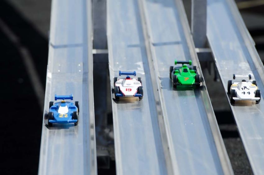 Four wooden race cars race down a metal track for the Pinewood Derby
