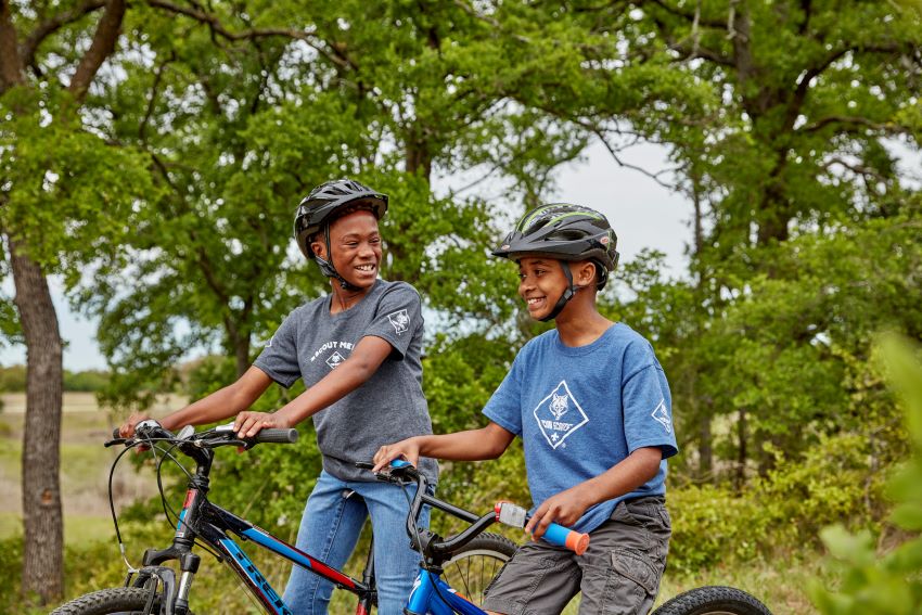 Scouts Biking Adventure | Outdoor Fun and Skill-Building for Youth. Two Scouts wearing helmets biking through a wooded trail, enjoying outdoor adventure and learning new skills.