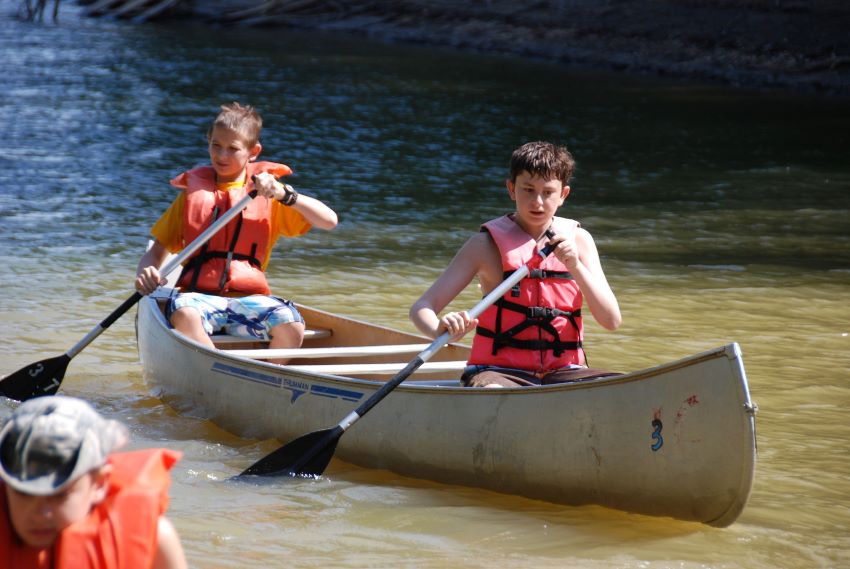 two boy scouts canoeing in a river at summer camp