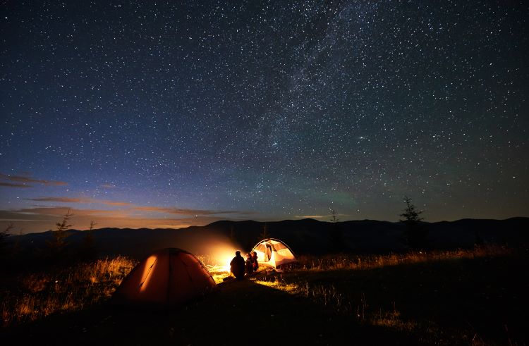 Family camps under the stars near a campfire and two tents in the Arizona outback