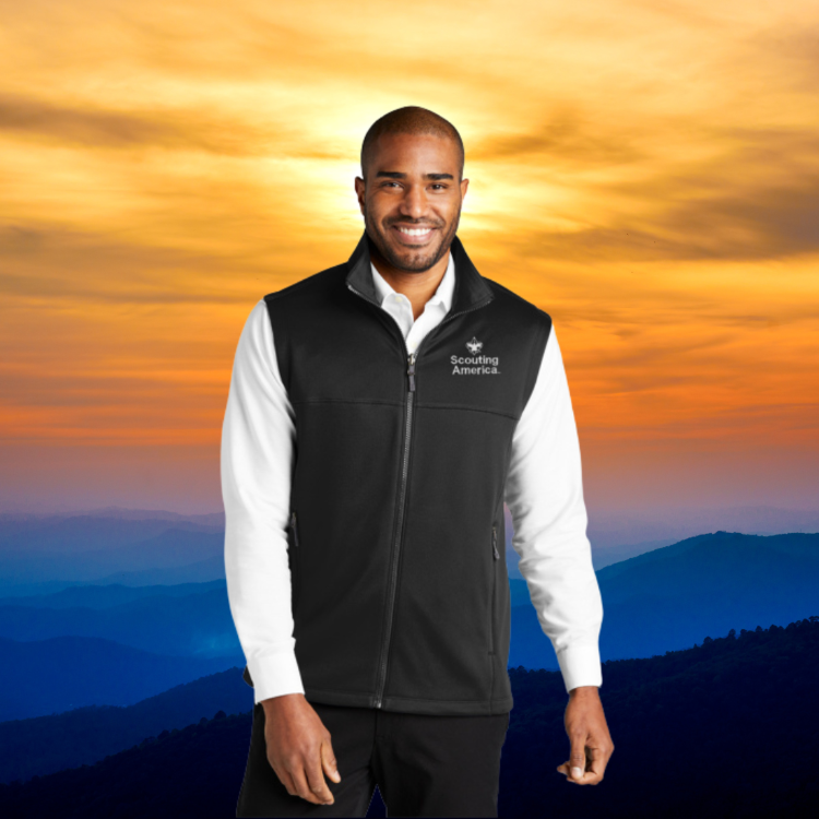 Scouting America Smooth Fleece Vest - Men's S-4XL A man wearing a black Scouting America Smooth Fleece Vest over a white shirt, standing against a scenic mountain sunset.